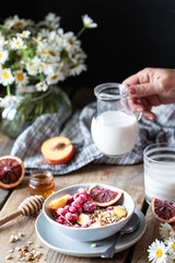 Granola breakfast with berries and fruits and honey and a glass of milk or yogurt on a wooden table. Bouquet of daisies. rustic