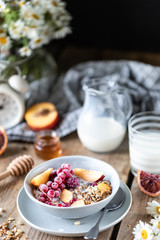 Granola breakfast with berries and fruits and honey and a glass of milk or yogurt on a wooden table. Bouquet of daisies. rustic