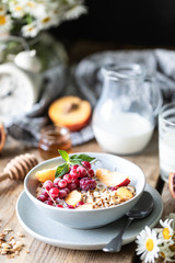 Granola breakfast with berries and fruits and honey and a glass of milk or yogurt on a wooden table. Bouquet of daisies. rustic