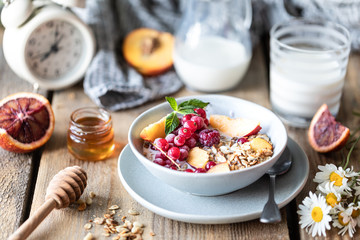 Granola breakfast with berries and fruits and honey and a glass of milk or yogurt on a wooden table. Bouquet of daisies. rustic