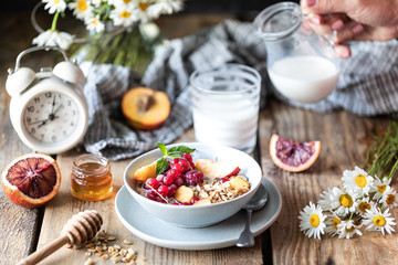 Granola breakfast with berries and fruits and honey and a glass of milk or yogurt on a wooden table. Bouquet of daisies. rustic