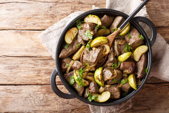 German food fried beef liver with green apples and onions close-up in a pan. Horizontal top view