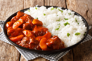 Spicy beef cooked with apples in tomato sauce with rice side dish close-up on a plate. horizontal