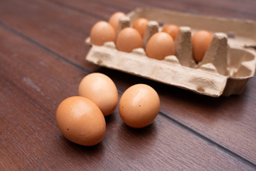 Close up of organic raw chicken eggs in egg box on brown wooden floor background