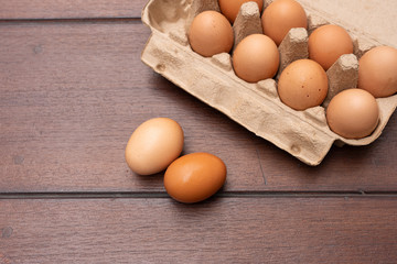 Close up of organic raw chicken eggs in egg box on brown wooden floor background