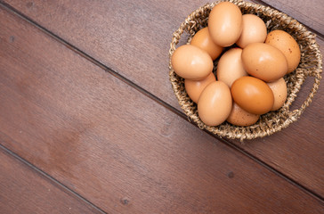 Top view close up of organic raw chicken eggs in basket on brown wooden floor background