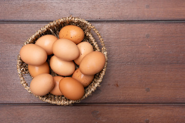 Top view close up of organic raw chicken eggs in basket on brown wooden floor background