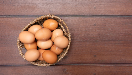 Top view close up of organic raw chicken eggs in basket on brown wooden floor background