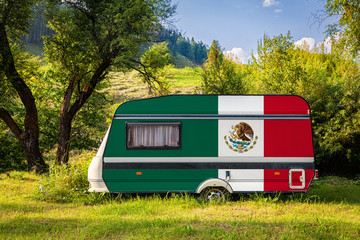 A car trailer, a motor home, painted in the national flag of Mexico stands parked in a mountainous. The concept of road transport, trade, export and import between countries. 