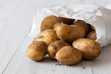 New potatoes in a white paper bag, environmentally friendly biodegradable packaging, with a grey wood background