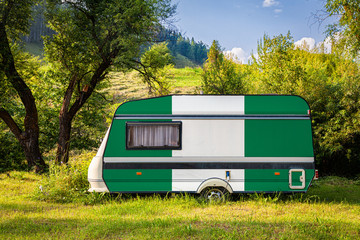 A car trailer, a motor home, painted in the national flag of Nigeria stands parked in a mountainous. The concept of road transport, trade, export and import between countries. 
