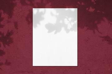 Empty white vertical rectangle poster mockup with soft shadow on dark red colored concrete wall background. Flat lay, top view