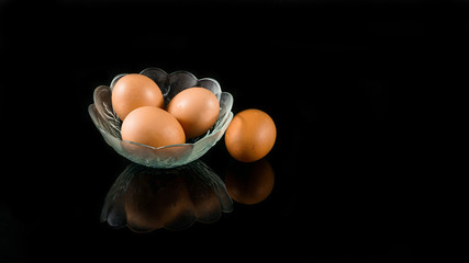 three egg inside a bowl with one outside isolated in black with reflection below