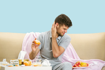 Young man suffering from allergy to citrus fruits. Having skin rash, itching, Sneezing in the napkin, sitting surrounded by grapefruits and oranges. Taking medicine with no result. Healthcare concept.