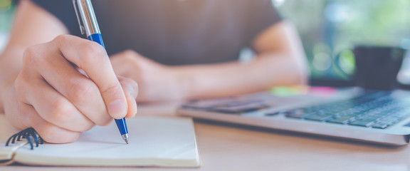 Woman hand is writing on a notepad with a pen in office.Web banner.