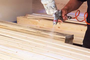 A man covers wooden boards with varnish in the workshop with a spray.