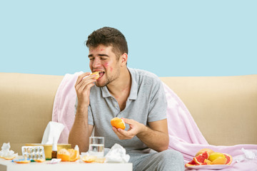 Young man suffering from allergy to citrus fruits. Having skin rash, itching, Sneezing in the napkin, sitting surrounded by grapefruits and oranges. Taking medicine with no result. Healthcare concept.