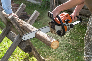 The employee produces a chainsaw sawing wood parts on a special device, outdoors, in the yard