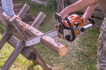 The employee produces a chainsaw sawing wood parts on a special device, outdoors, in the yard,...