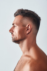 Fototapeta premium Confident and handsome. Side view of charming man with a stubble standing against grey background