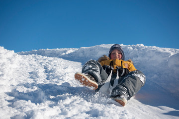 Fototapeta na wymiar Boy sliding down a hill in the snow in winter