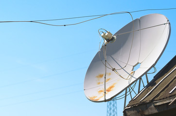 Old Satellite Television Antenna Dish on Top of a Barn Roof Covered with Waterproofing Tar Paper against Summer Blue Sky.
