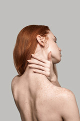 Elegant beauty. Back view of young and beautiful redhead woman touching her neck while standing...