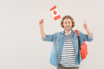 Young male student with Canadian flag on light background