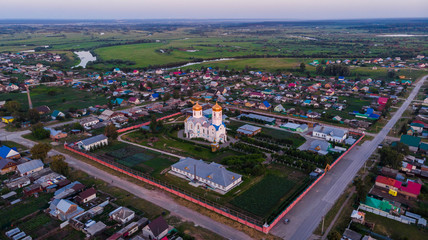Naklejka premium Aerial shot. Alexander Nevsky Temple in the center of the village, with many different houses around. Bright summer evening 