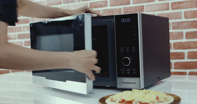 Close up scene video of someone putting full load topping pizza into microwave oven, he setting time to cook it.