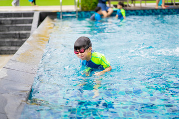 A boy is playing and swimming at the swimming pool in the evening.