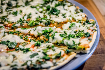 Vegetarian spinach pizza  in close-up on a plate, with cheese topping, one slice cut out