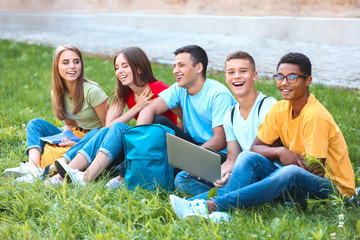 Obraz premium Portrait of young students with laptop sitting on grass outdoors