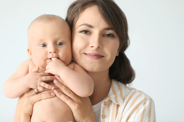 Happy mother with cute little baby on light background