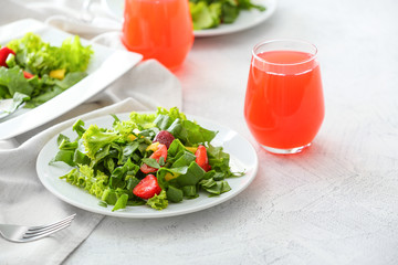 Plates with fresh tasty salad and glasses of juice on table