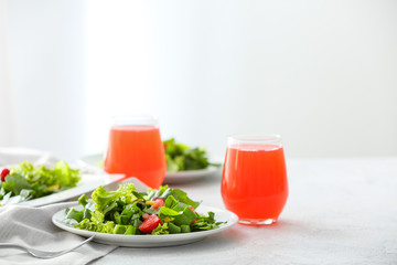 Plates with fresh tasty salad and glasses of juice on table