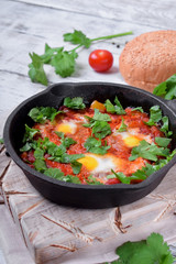 Shakshuka with tomato sauce and quail eggs topped with cilantro in a cast iron pan. Jewish cuisine meal