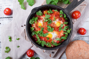 Shakshuka with tomato sauce and quail eggs topped with cilantro in a cast iron pan. Jewish cuisine meal
