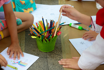 detail of children's hands painting with different colored paints on blank sheets sitting on the floor