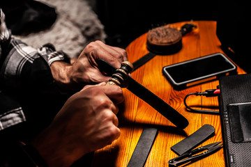 Man makes a leather product, and polishes it in a home workshop. On a wooden table.