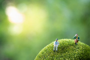 Miniature people: business people sitting on a green moss stone, doing activity and discussing ideas, society and teamwork concept. - obrazy, fototapety, plakaty