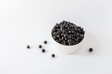 Fototapeta na wymiar Ripe black currant or blueberries in a small white Cup on a white background. Black currant harvest. Healthy food. vegetarian food