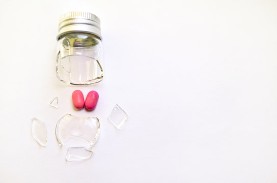 A broken small glass bottle with a metal cap, two pink heart-shaped tablets fell out of it, on a white background