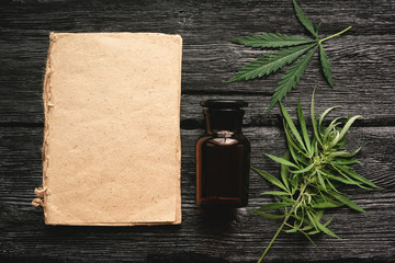 Cannabis cbd oil recipe blank book with a copy space, cbd oil in a bottle and green leaves on a black wooden table background.