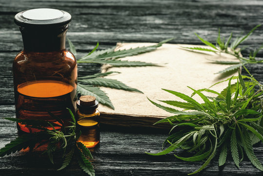 Cannabis cbd oil recipe blank book with a copy space, cbd oil in a bottle and green leaves on a black wooden table background.
