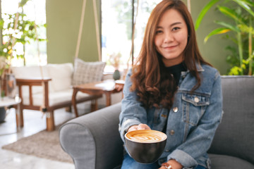 Closeup image of a beautiful asian woman holding and giving a cup of hot coffee in cafe