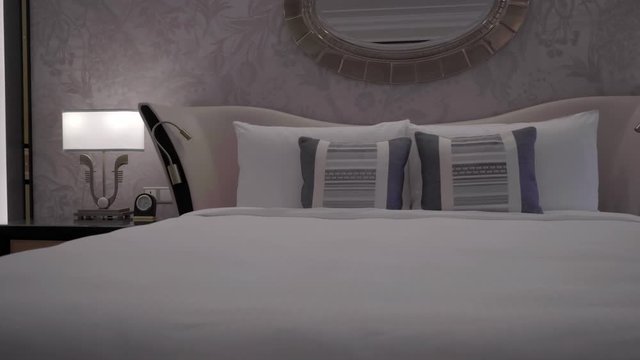 Luxury king size bed in a grand hotel room with dim lights, panning shot