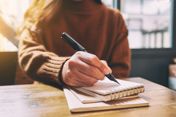 Closeup image of a woman writing on blank notebook with fountain pen on wooden table