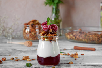 Layered breakfast with granola, yogurt and jam topped with raspberries in a glass jar on the white table