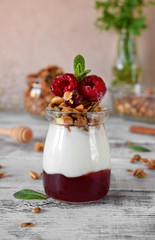 Layered breakfast with granola, yogurt and jam topped with raspberries in a glass jar on the white table